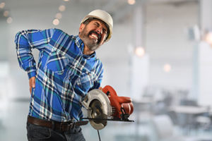 Male construction worker touches his lower back and winces in pain.  